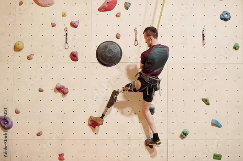 Obraz na płótnie Back view of young disabled sportsman with robotic leg climbing wall