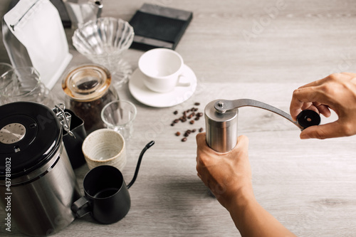 Close up, Barista use grinder coffee beans with manual stainless steel grinding to make black coffee machine, brewing equipment or coffee drip set Dripper on a wooden table In the kitchen at home