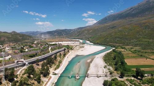 Wild river of Vjosa streaming through mountains near stone walls of fortress in Tepelena photo