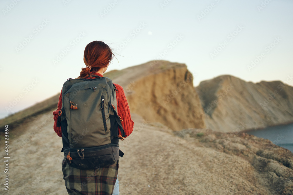 beautiful woman in the mountains in nature with a backpack on her back near the sea