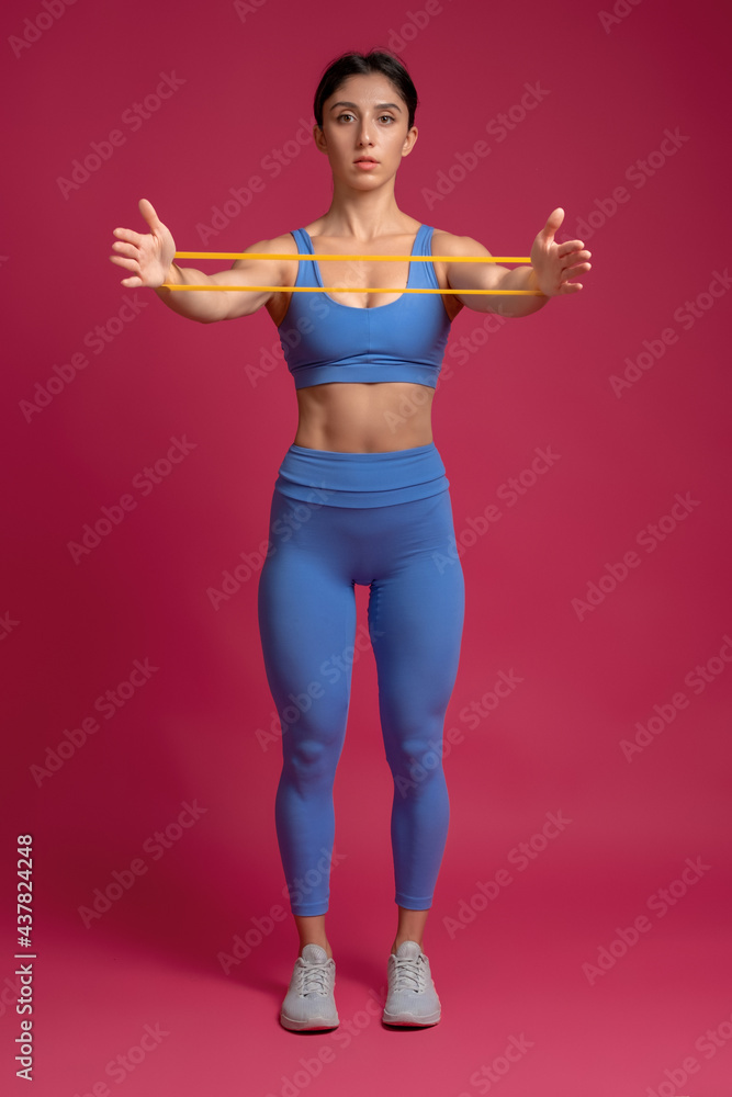 Woman doing arm and shoulder exercises with resistance band on maroon background Woman doing arm and shoulder exercises with resistance band on maroon background