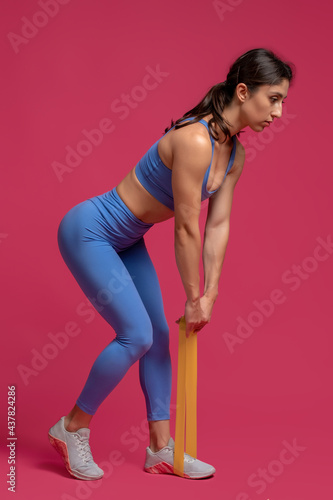 Girl doing resistance band deadlifts on maroon background