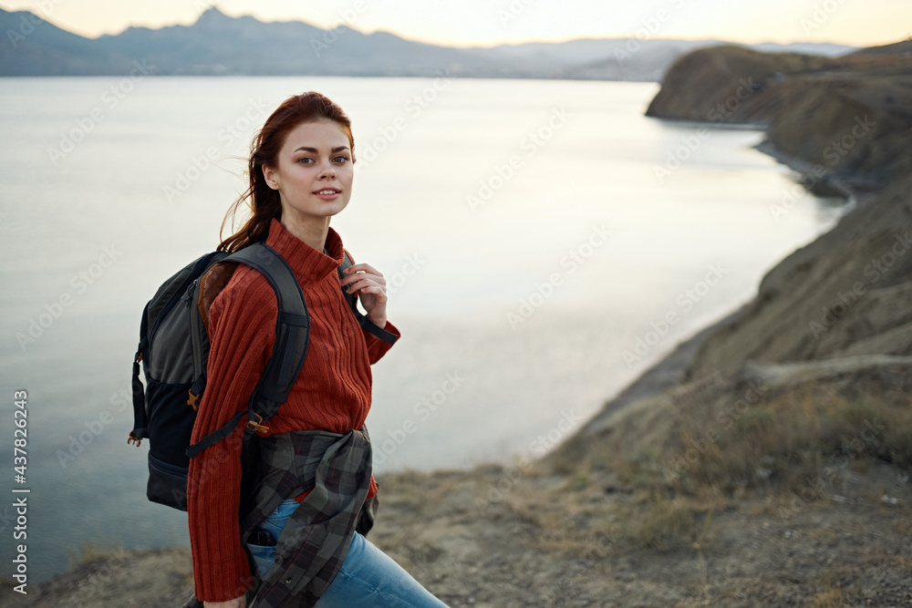 woman in a red sweater with a backpack on her back in the mountains on nature high rocks landscape sunset