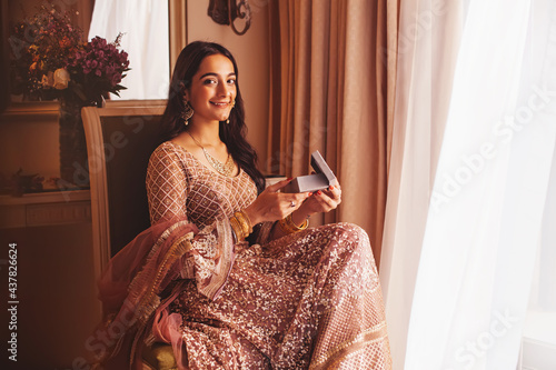 Beautiful Indian woman in a fancy traditional outfit opening the box with present in the luxury five star hotel room, looking at camera