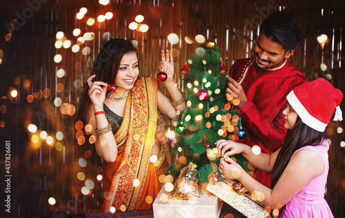 Beautiful Indian family in ethnic clothes decorating Christmas tree for the New Year celebration at night