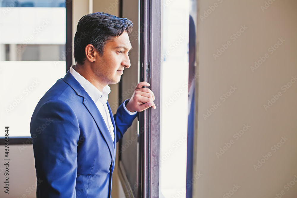 Handsome young sad Indian man in formal suit looking from the window Handsome young sad Indian man in formal suit looking from the window