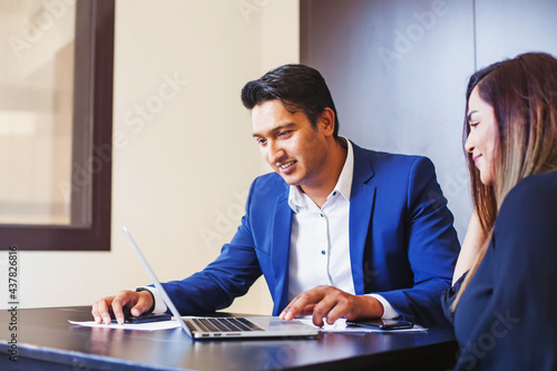 Handsome young Indian professional working on a laptop, training his colleague 
