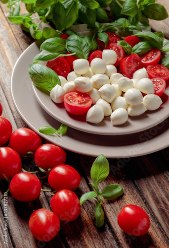 Caprese salad with tomato, mini mozzarella and basil on a old wooden table.