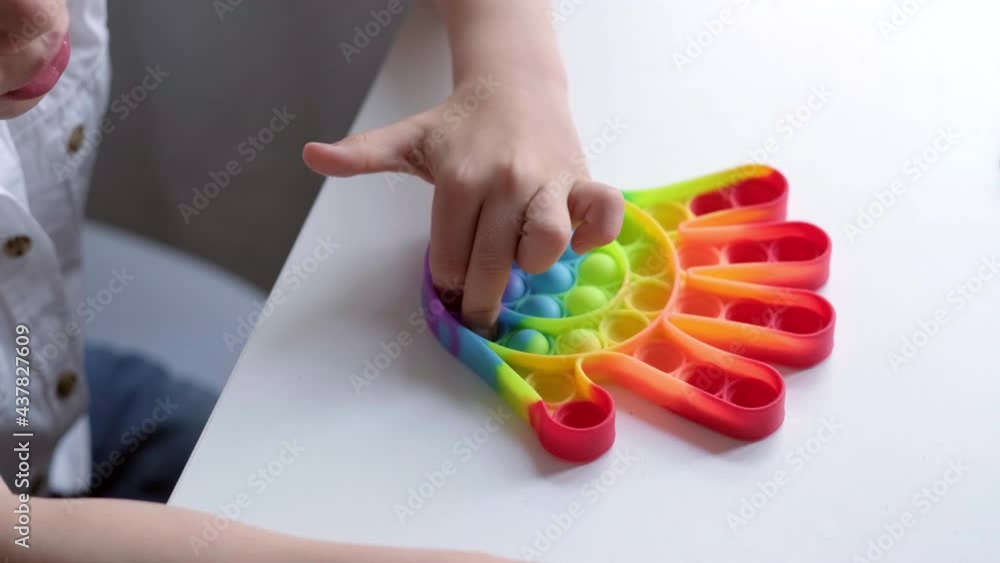Child play with pop it sensory toy. Boy presses on colorful rainbow squishy soft silicone bubbles. Stress and anxiety relief. Trendy fidgeting game for stressed children and adults Child play with pop it sensory toy. Boy presses on colorful rainbow squishy soft silicone bubbles. Stress and anxiety relief. Trendy fidgeting game for stressed children and adults