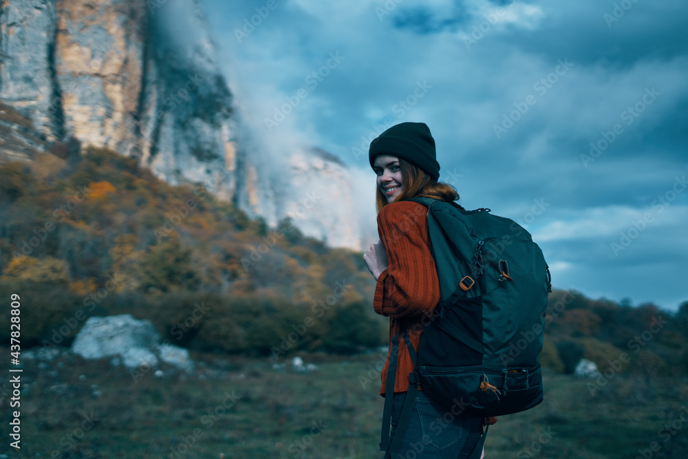 woman traveler in a sweater with a backpack on her back in autumn in the mountains on nature and sky clouds woman traveler in a sweater with a backpack on her back in autumn in the mountains on nature and sky clouds