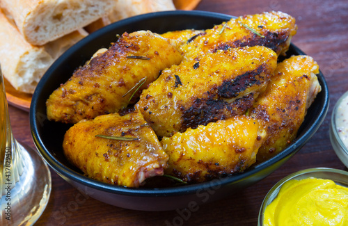 Black bowl of appetizing roasted chicken wings with two kinds of sauce