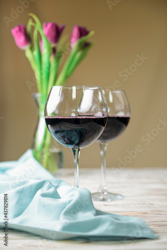 Two glasses of red wine and tulips on a wooden background.