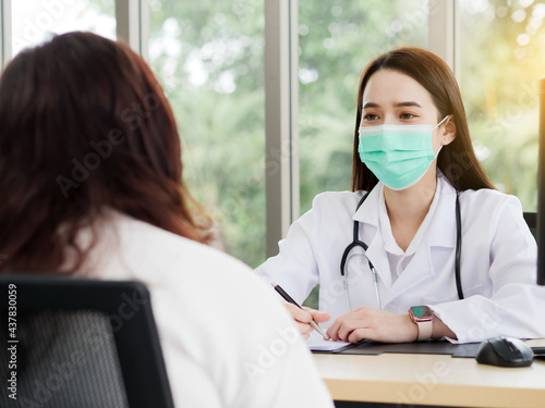 A female doctor or nurse with a smiling face under the surgical mask is talking or interview a middle-aged female patient at the workplace, ideas for healthcare concepts. 