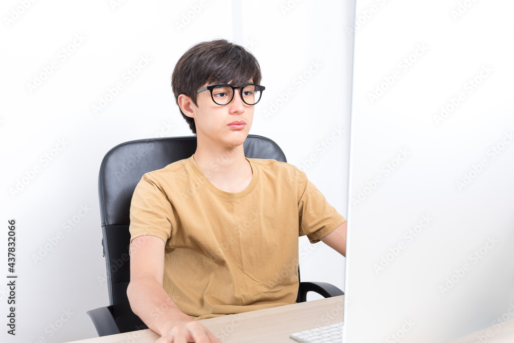 Serious teenage boy sitting on the chair while using computer at home. Online learning with his school classmates during lockdown.
