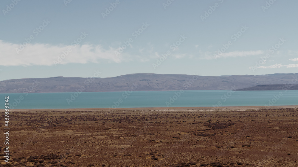 Minimalist Landscape with Blue River, Line of Sandy Beach, Mountains and Evening Sky. Mountain Horizon. Calm Water Surface and Sky with Soft Clouds. Nearby El Chalten, Argetina. Las Vueltas River. Minimalist Landscape with Blue River, Line of Sandy Beach, Mountains and Evening Sky. Mountain Horizon. Calm Water Surface and Sky with Soft Clouds. Nearby El Chalten, Argetina. Las Vueltas River.
