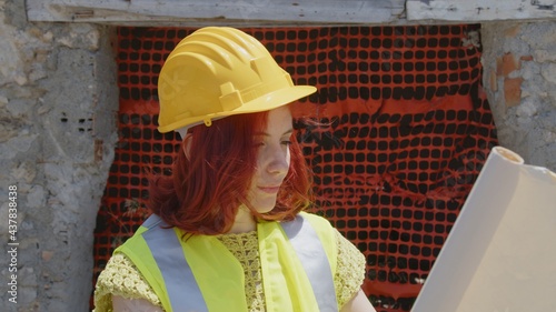 Giovane ragazza ingegnere con caschetto giallo guarda il progetto di fronte al cantiere 