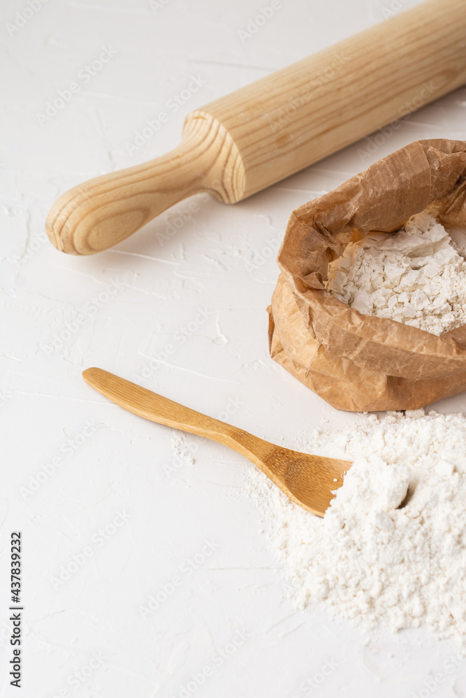 Top view of a pile of flour with wooden spoon, bag with flour and rolling pin, with selective focus, white background, vertical, with copy space