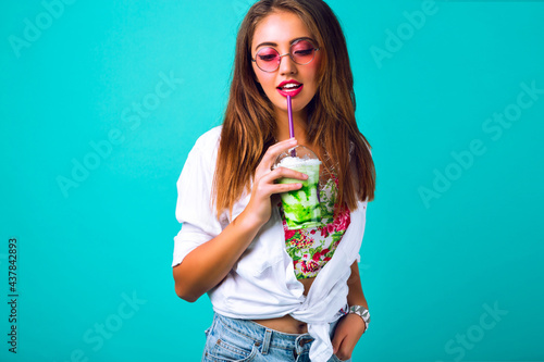 Young sexy hipster woman in mini denim shorts drinking tasty smoothie