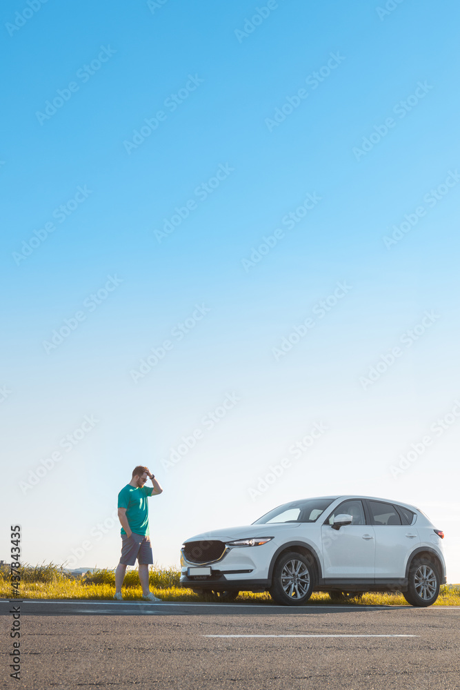 man traveler standing near car at roadside of speedway at sunset