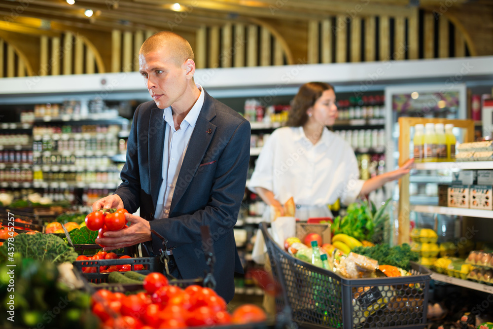 Young confident man carefully selects fresh vegetables on the counter in the supermarket