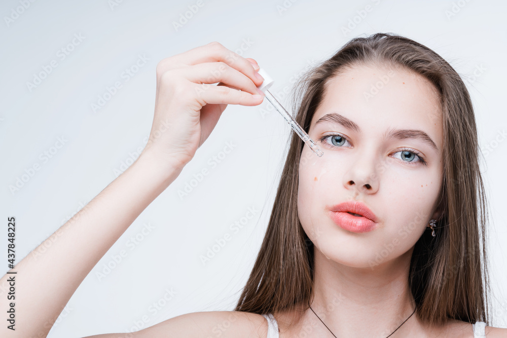 Beautiful young girl holding a dropper with serum in her hands, applying it to her face Beautiful young girl holding a dropper with serum in her hands, applying it to her face