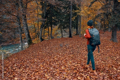 woman with backpack hiking travel in autumn park tall trees river fallen leaves