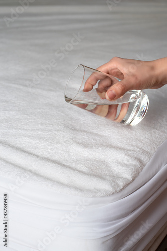 Woman's hand with a glass of water above the mattress in a waterproof case
