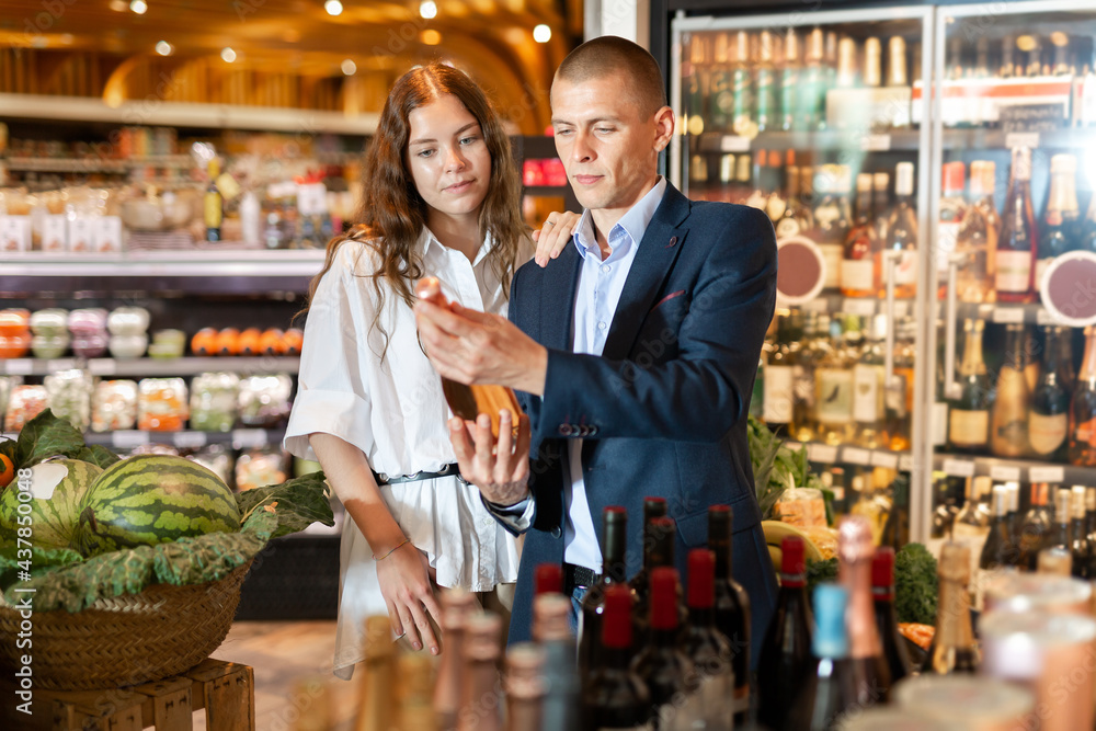 Portrait of young family pair choosing bottle of wine for dinner in supermarket