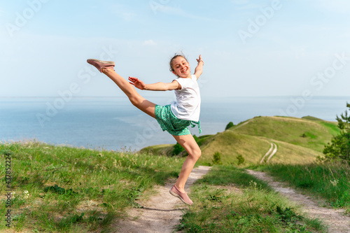 A little girl child cheerfully jumps into the air on a path in the middle of green meadows © KseniaJoyg