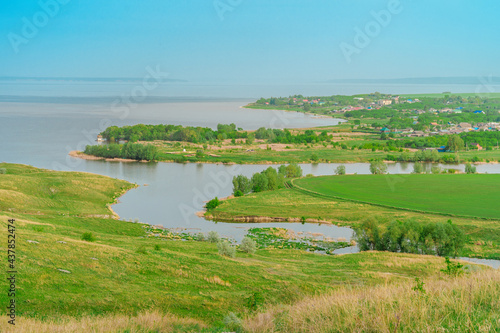 Spring and summer landscape. Green meadows with trees and a river in the background