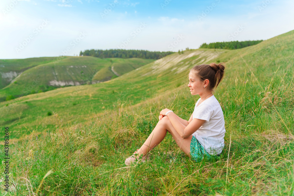 Beautiful little baby girl sitting on a green meadow with a delightful view of the hilly landscape Beautiful little baby girl sitting on a green meadow with a delightful view of the hilly landscape