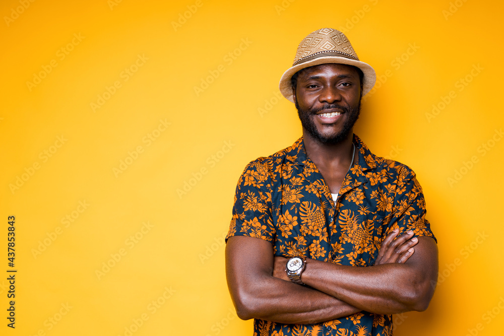 Cheerful african american man in summer shirt and hat crossing his arms on his chest smiling