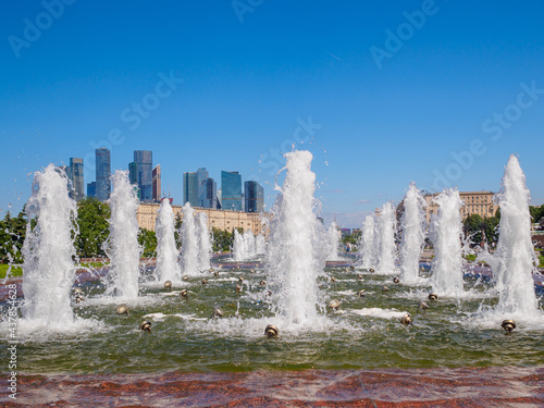 Jets of fountains on a sunny day against the backdrop of modern skyscrapers and a cloudless blue sky. Recreation area in Victory Park on Poklonnaya Hill in summer.