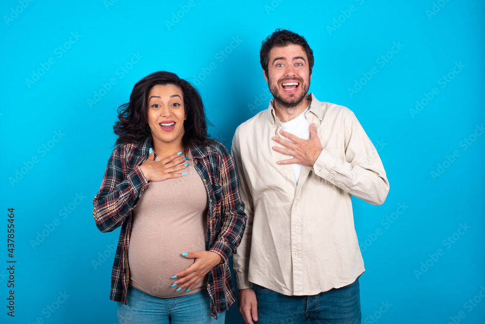 young couple expecting a baby standing against blue background smiles toothily cannot believe eyes expresses good emotions and surprisement young couple expecting a baby standing against blue background smiles toothily cannot believe eyes expresses good emotions and surprisement