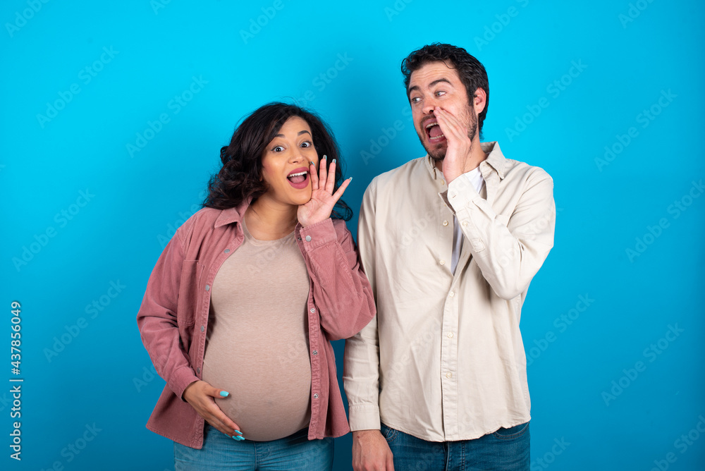 young couple expecting a baby standing against blue background hear incredible private news impressed scream share young couple expecting a baby standing against blue background hear incredible private news impressed scream share
