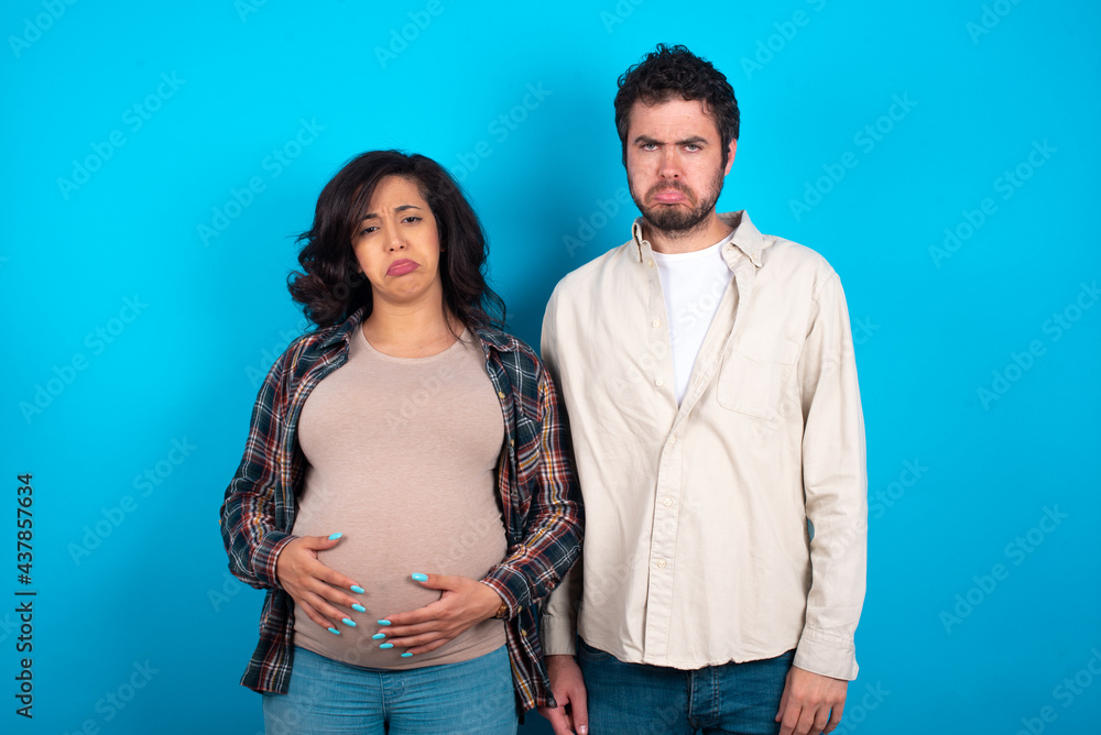 young couple expecting a baby standing against blue background depressed and worry for distress, crying angry and afraid. Sad expression. young couple expecting a baby standing against blue background depressed and worry for distress, crying angry and afraid. Sad expression.