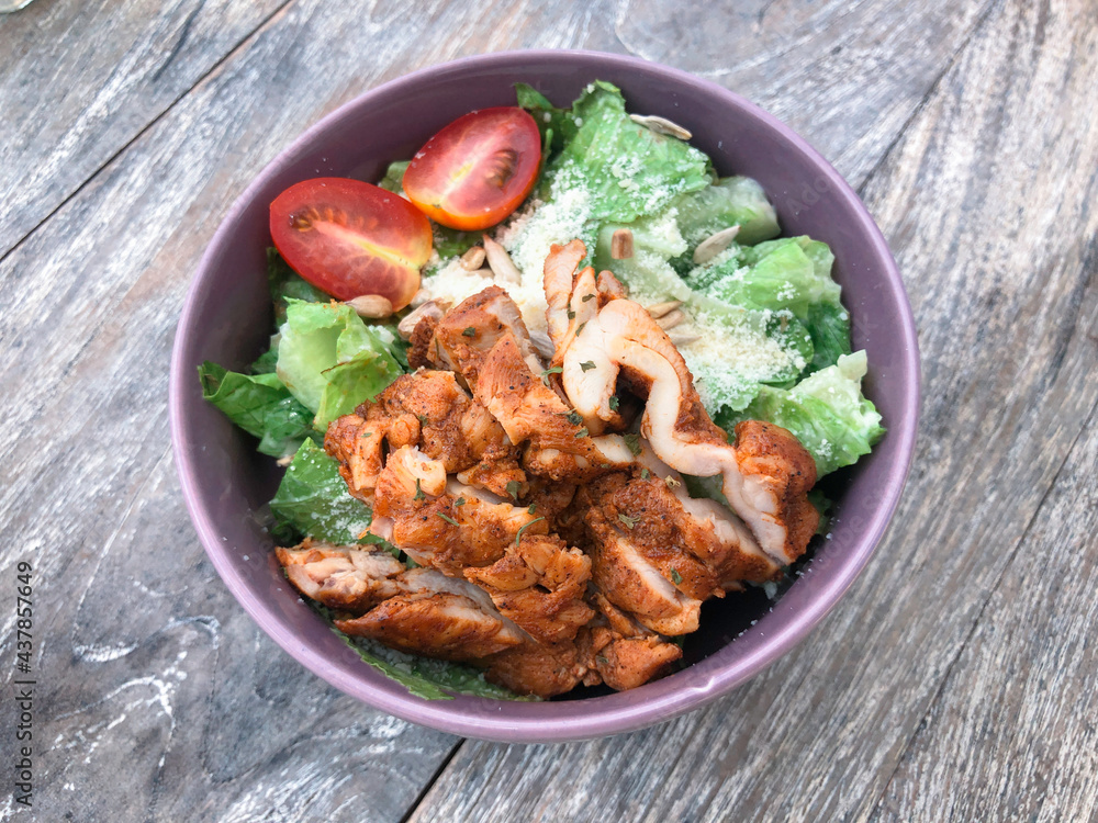 Fototapeta premium Green vegan salad from green leaves mix, vegetables, slices of chicken katsu. Top view on gray wood table.