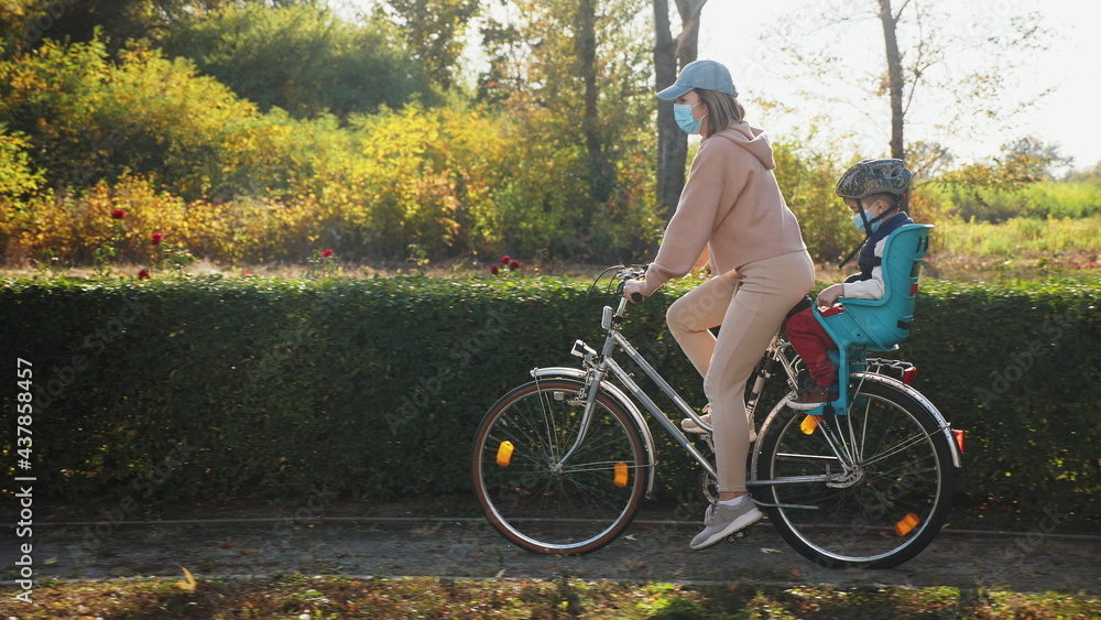 Fototapeta premium Mom and little son wears medical masks ride a bike in the park