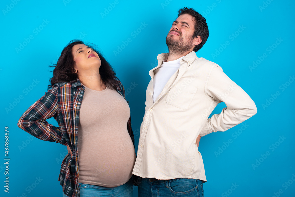 Obraz premium young couple expecting a baby standing against blue background got back pain