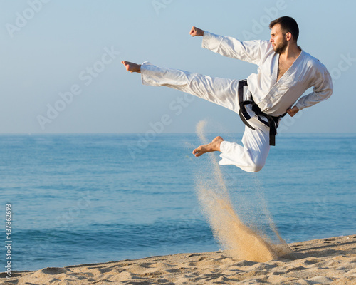 young man practicing karate positions at ocean quay in sunset