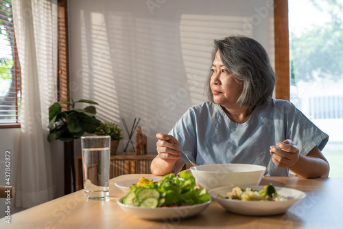 Unhappy Senior Elderly older grandmother eat alone on table in house.