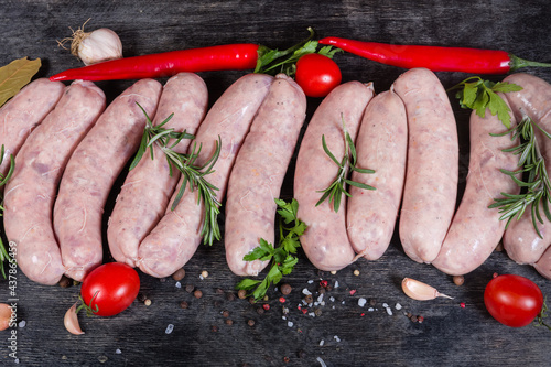 Raw pork sausages among spices and vegetables on dark surface
