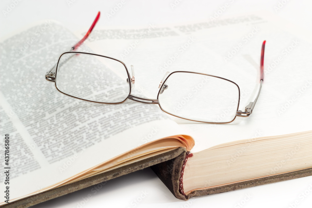 Eyeglasses in metal frame on open book with blurred text Eyeglasses in metal frame on open book with blurred text