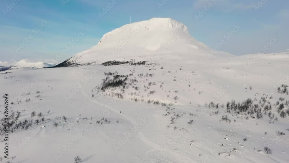 Aerial view of a snowmobile and a hiker heading towards the Saana fell, in lapland - tilt drone shot Aerial view of a snowmobile and a hiker heading towards the Saana fell, in lapland - tilt drone shot