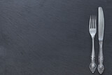 Silver - colored cutlery-knife and fork on a black background with a copy of the space