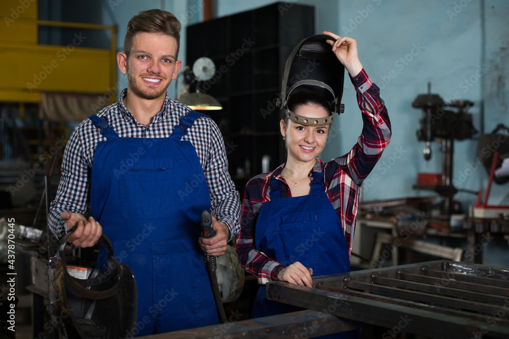 Man with young woman are standing near table and working together in workshop.