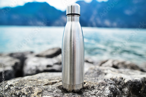 Close-up of steel eco thermo water bottle on the background of the lake in the mountains. Copy space. Zero waste, no plastic. Reusable water bottle. Stainless steel reusable water bottle. 