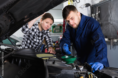 Two workers are replacing the oil in the car on their workplace in workshop.