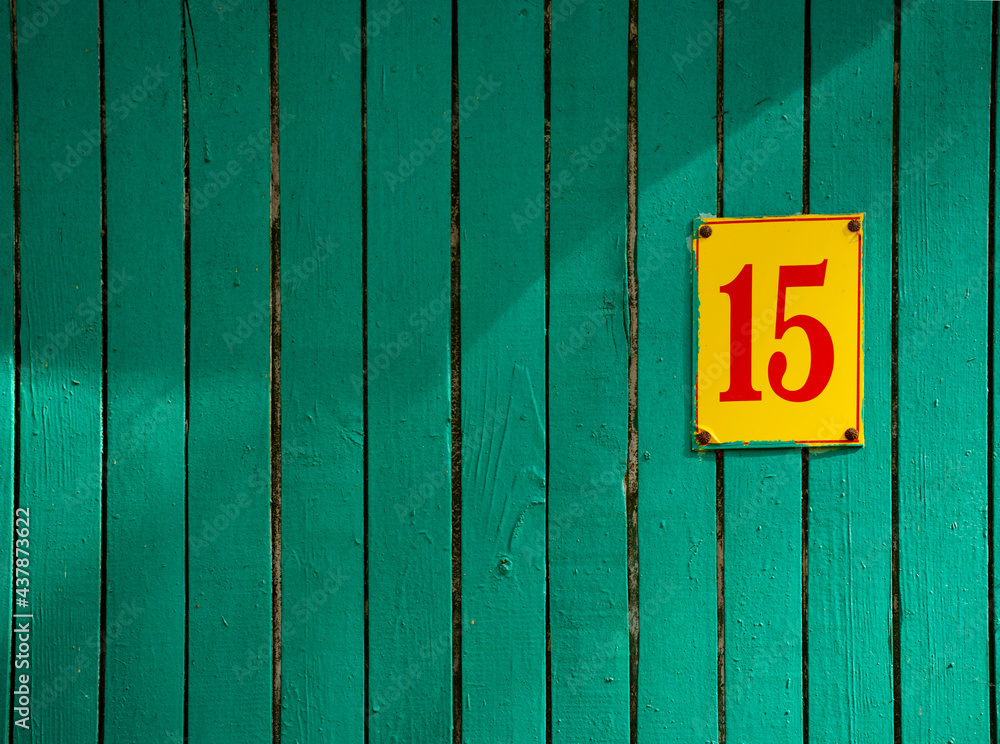 Green flaky paint on an old weathered wooden wall with plate number fiveteen. Wood wall with shadows. Peeling paint flakes. Green flaky paint on an old weathered wooden wall with plate number fiveteen. Wood wall with shadows. Peeling paint flakes.