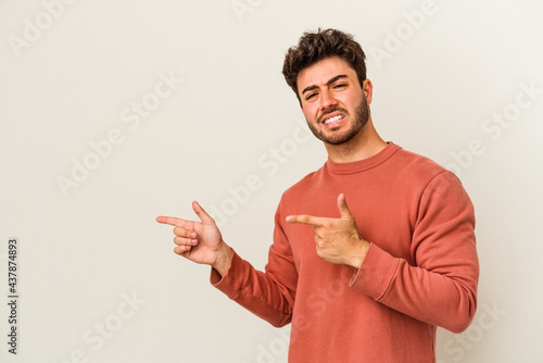 Young caucasian man isolated on white background shocked pointing with index fingers to a copy space.
